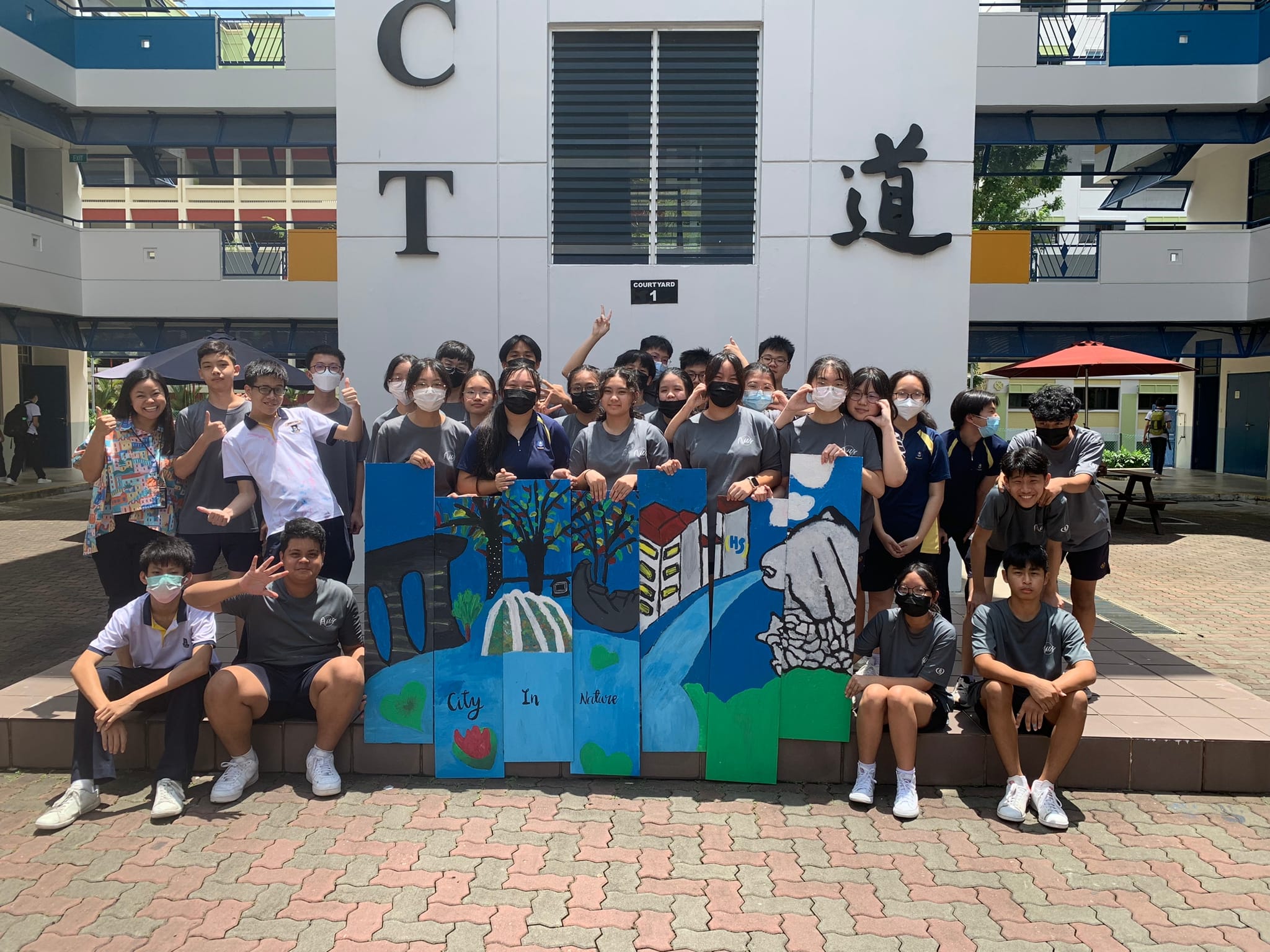 Group of students posing outdoors holding painted panels reading "City in Nature" with trees and buildings depicted.
